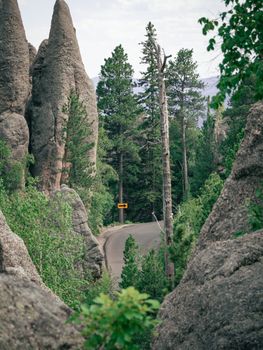 A scenic mountain road curves through dense forest and towering rock formations, offering a stunning nature landscape.