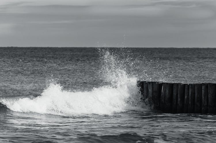 Grayscale Photo Of Sea Waves Crashing On Wooden Posts