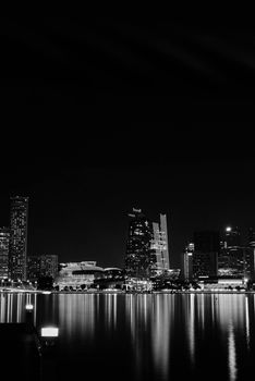 Black and white cityscape of the illuminated Singapore skyline at night reflecting on the waterfront.