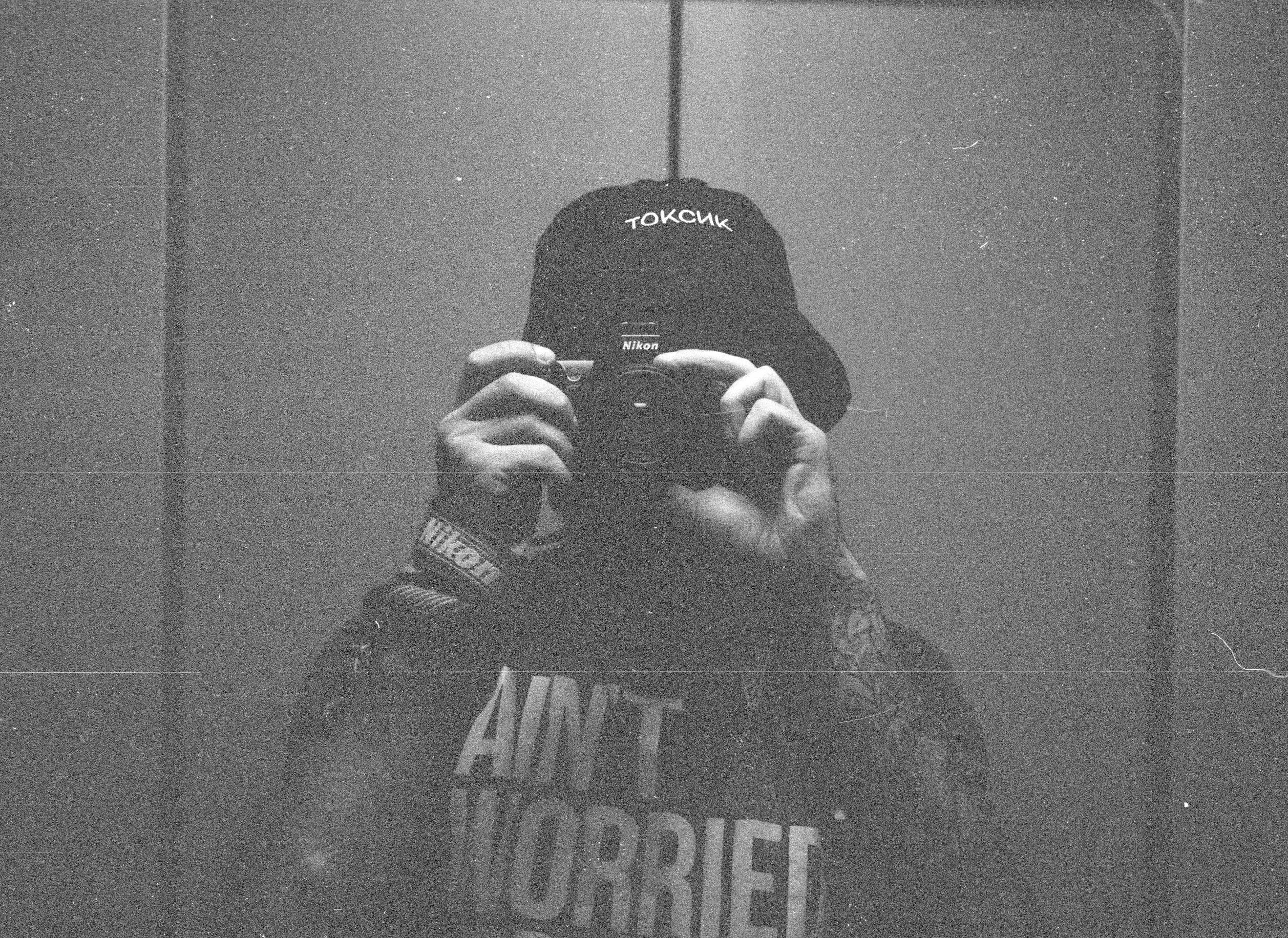 Grainy black and white image of photographer taking a self-portrait in reflection.