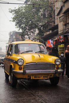 Classic yellow Ambassador taxi driving through a bustling Kolkata street.