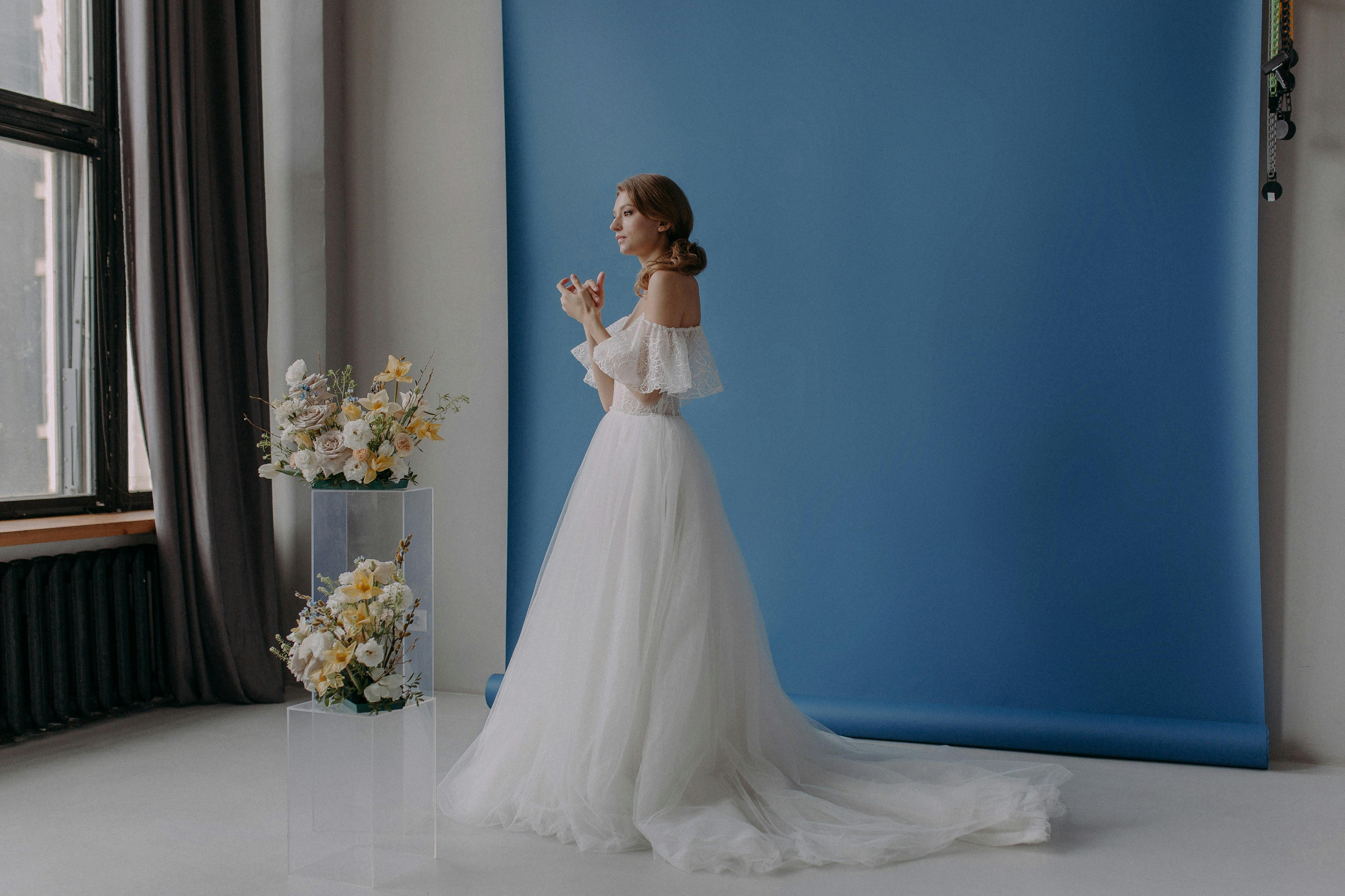 Elegant bride in a studio with blue backdrop and floral arrangements.