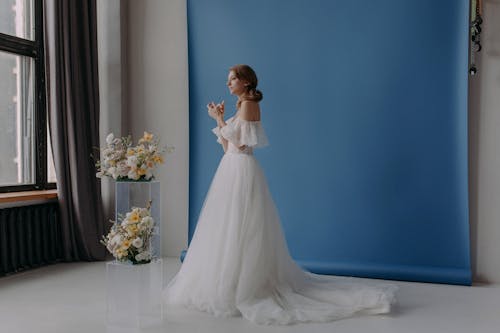 Woman in a White Gown Standing Near Flowers