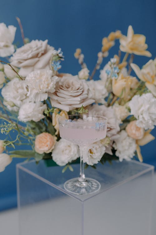 White Cocktail in a Crystal Glass on the Background of a Bouquet of Flowers