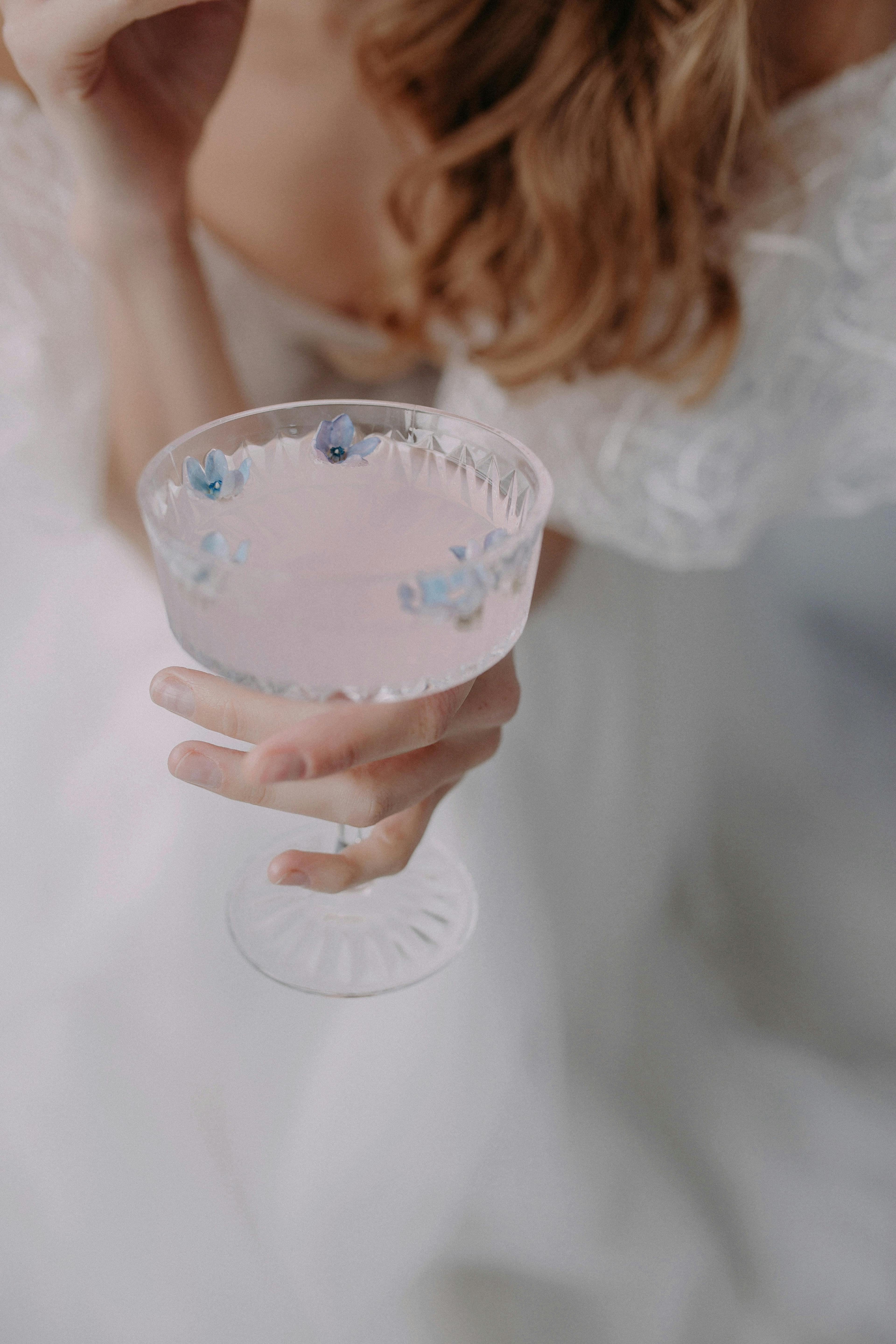 A woman adorned in white delicately holds a decorative crystal glass with blue flower embellishments.