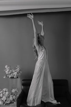 Black and white photo of a woman in an elegant dress, posing gracefully indoors.