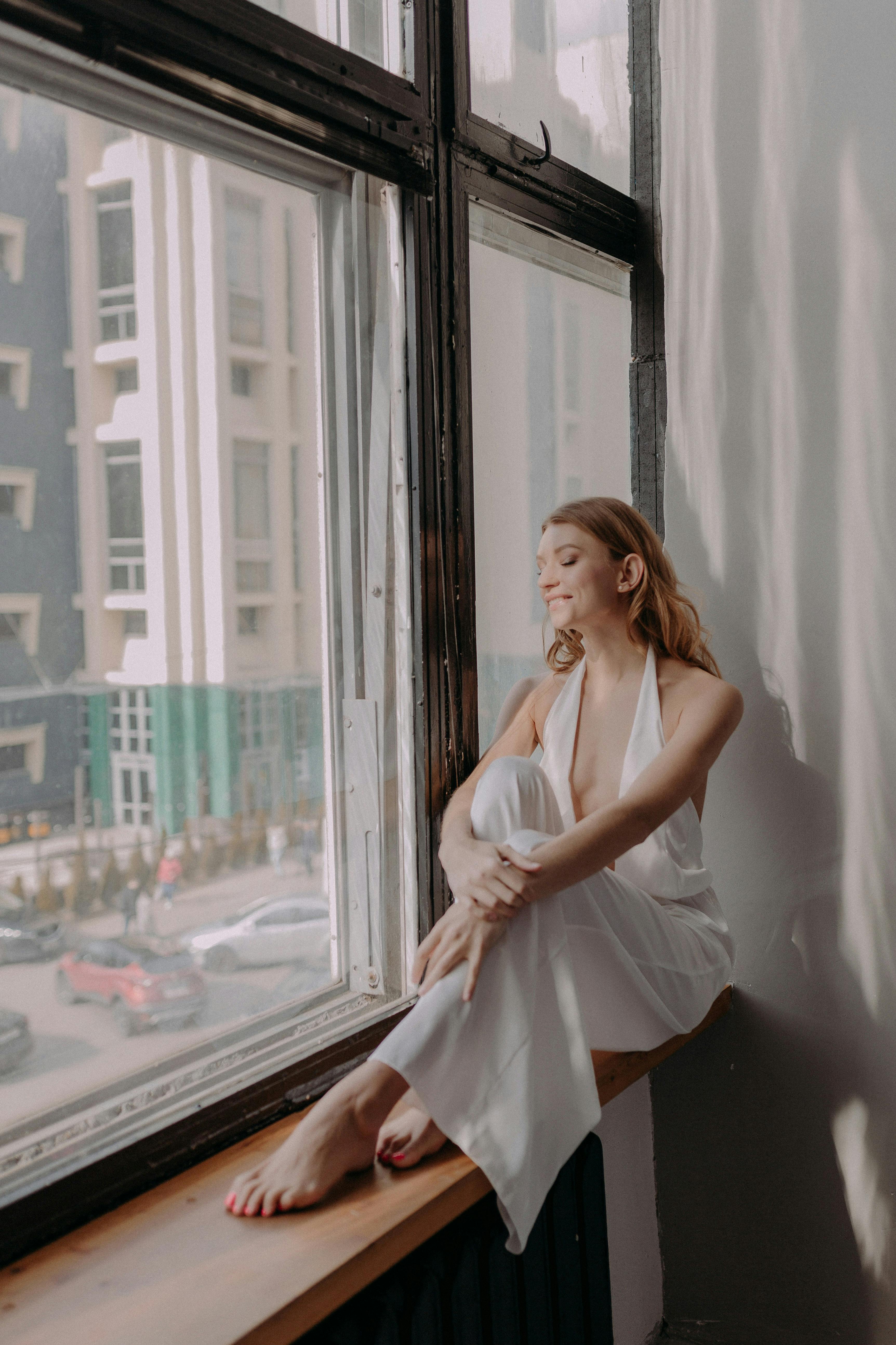 a woman in white dress sitting beside the glass window