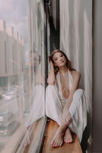 A serene portrait of a woman in a white dress sitting by a window, exuding elegance and calm.