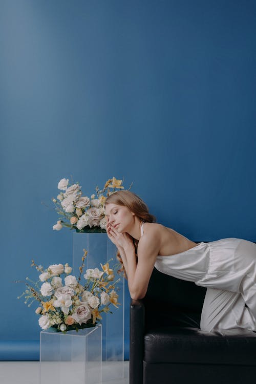 Model in a White Silk Outfit Posing on a Sofa next to Flowers