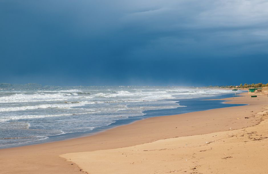 Tranquil beach view capturing waves gently rolling on the sandy shore under a dramatic sky in Pyrgos, Greece.