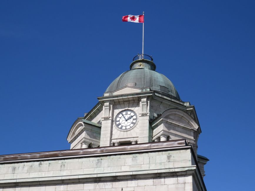 A classic domed building with a clock tower and Canadian flag against a clear blue sky.
