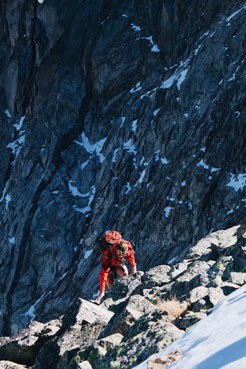 Person in Orange Jacket and Black Pants Standing on Rocky Mountain