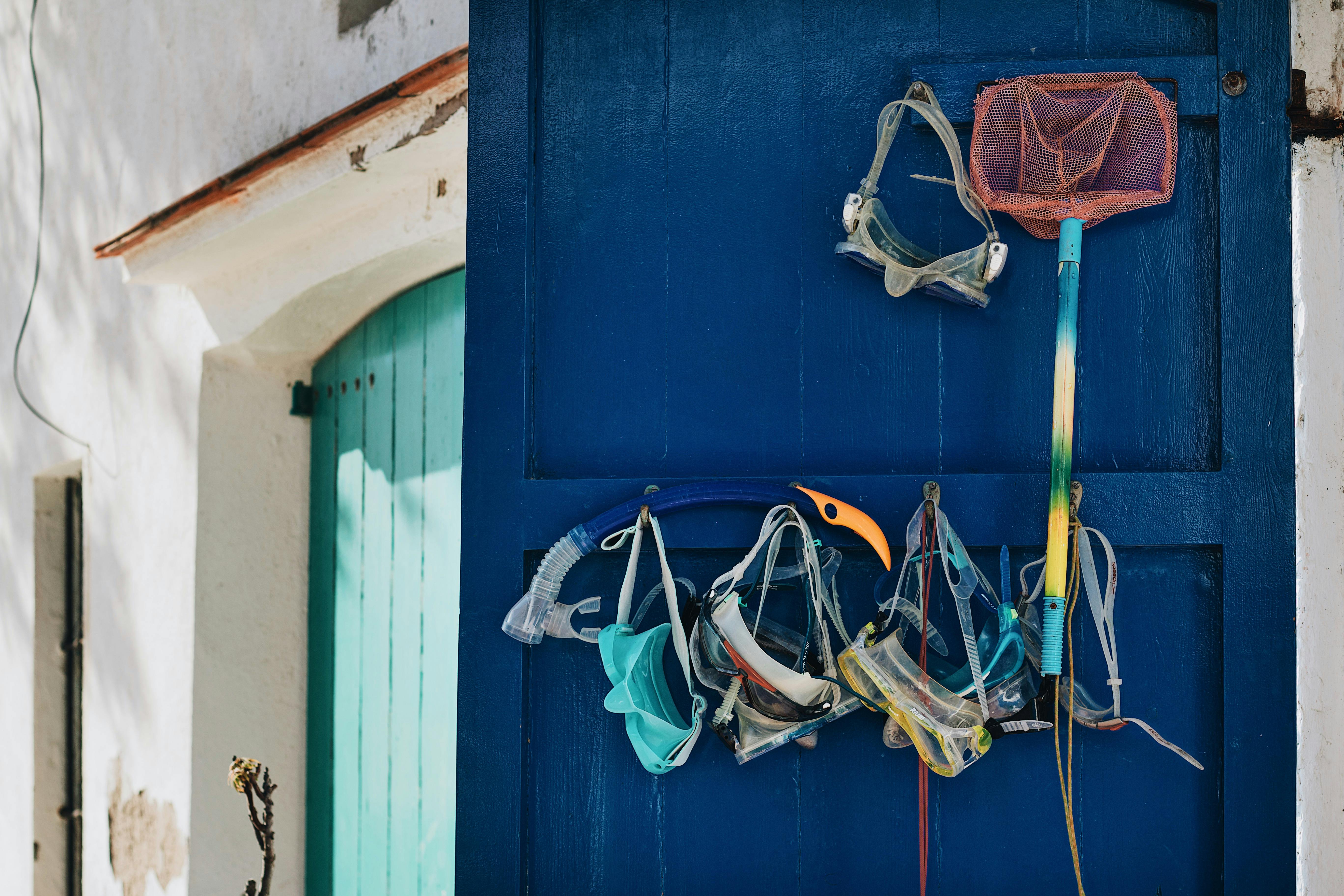 Snorkeling masks and equipment hanging on a vibrant blue door in an outdoor setting.