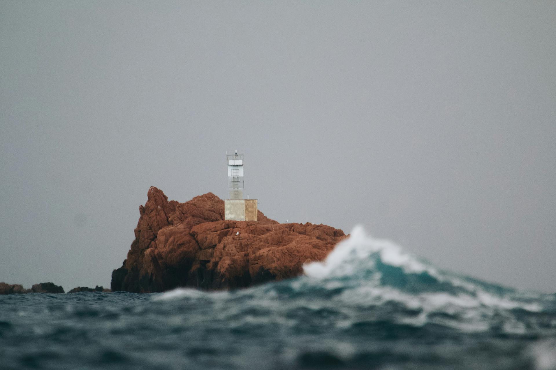 A peaceful lighthouse stands on a solitary rocky island surrounded by ocean waves.