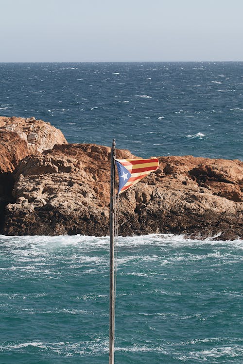 Orange and White Flag on Brown Rock Formation Near Body of Water