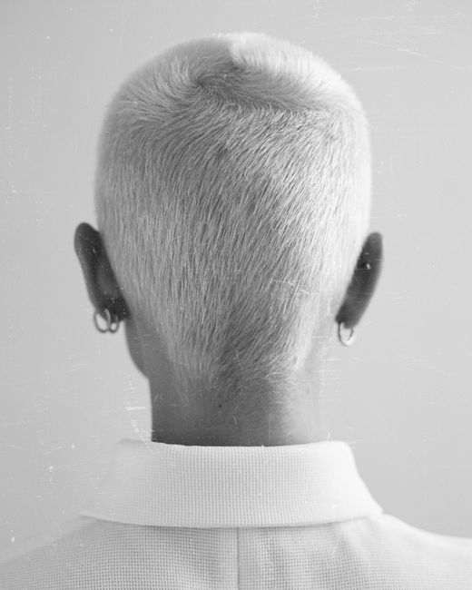 A black and white headshot showing the back view of a person with short, dyed hair.