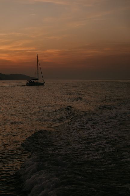 A tranquil seascape at sunset with a silhouette of a sailboat on the ocean.