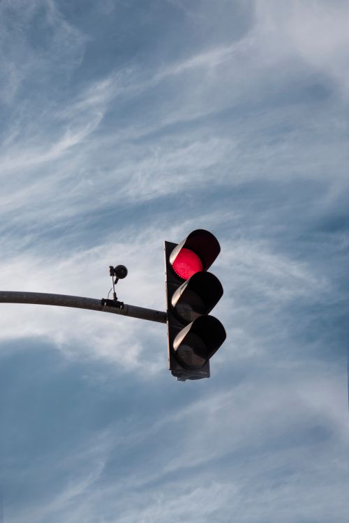 Free A low-angle shot of a red traffic light against a blue cloudy sky. Stock Photo