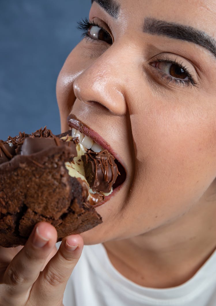 Photograph Of A Woman Biting A Chocolate Cake