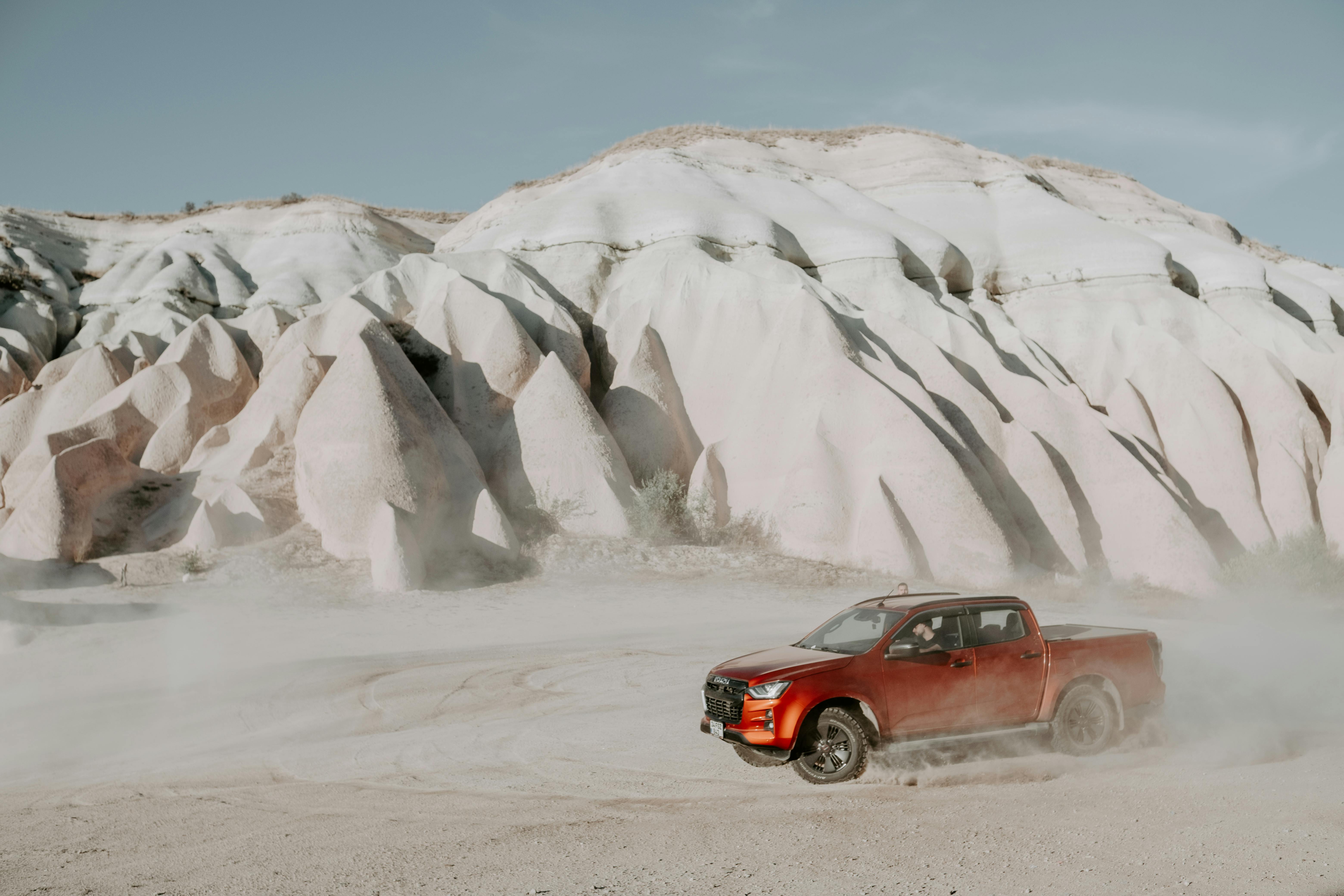 Dynamic shot of a red pickup truck off-roading through dusty desert with unique rock formations.