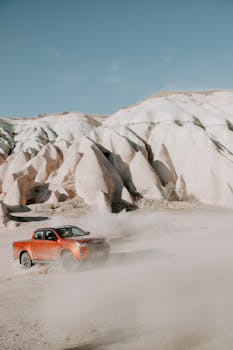 A red pickup truck driving through a stunning desert landscape with unique rock formations.