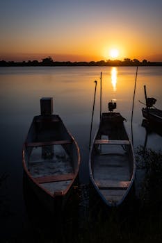 Peaceful sunrise over a river with moored boats reflecting in calm waters.