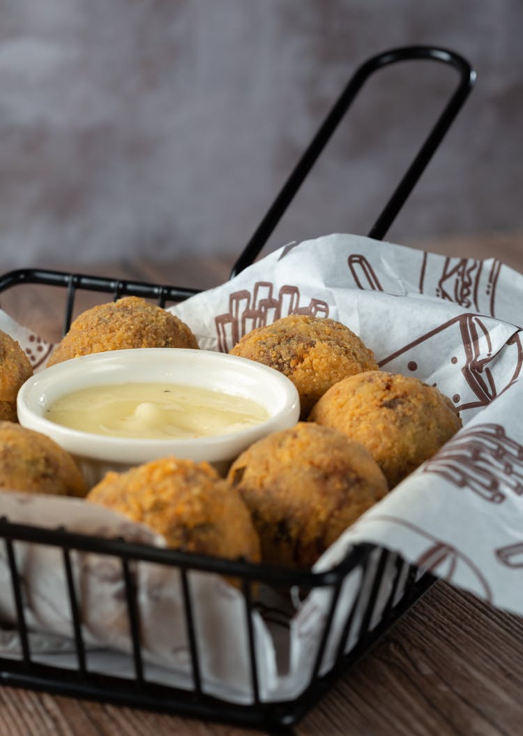 A Brown Fried Ball Shaped Food In A Basket With White Dip