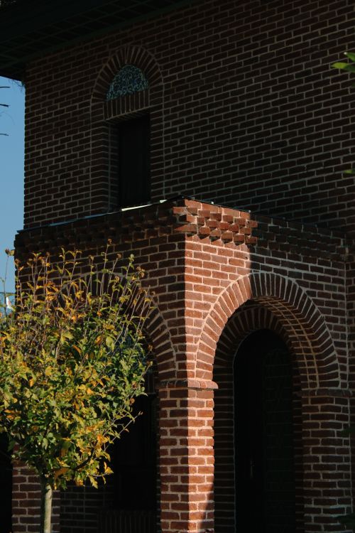 Free A timeless brick building facade featuring an elegant arch and window, framed by autumn foliage. Stock Photo