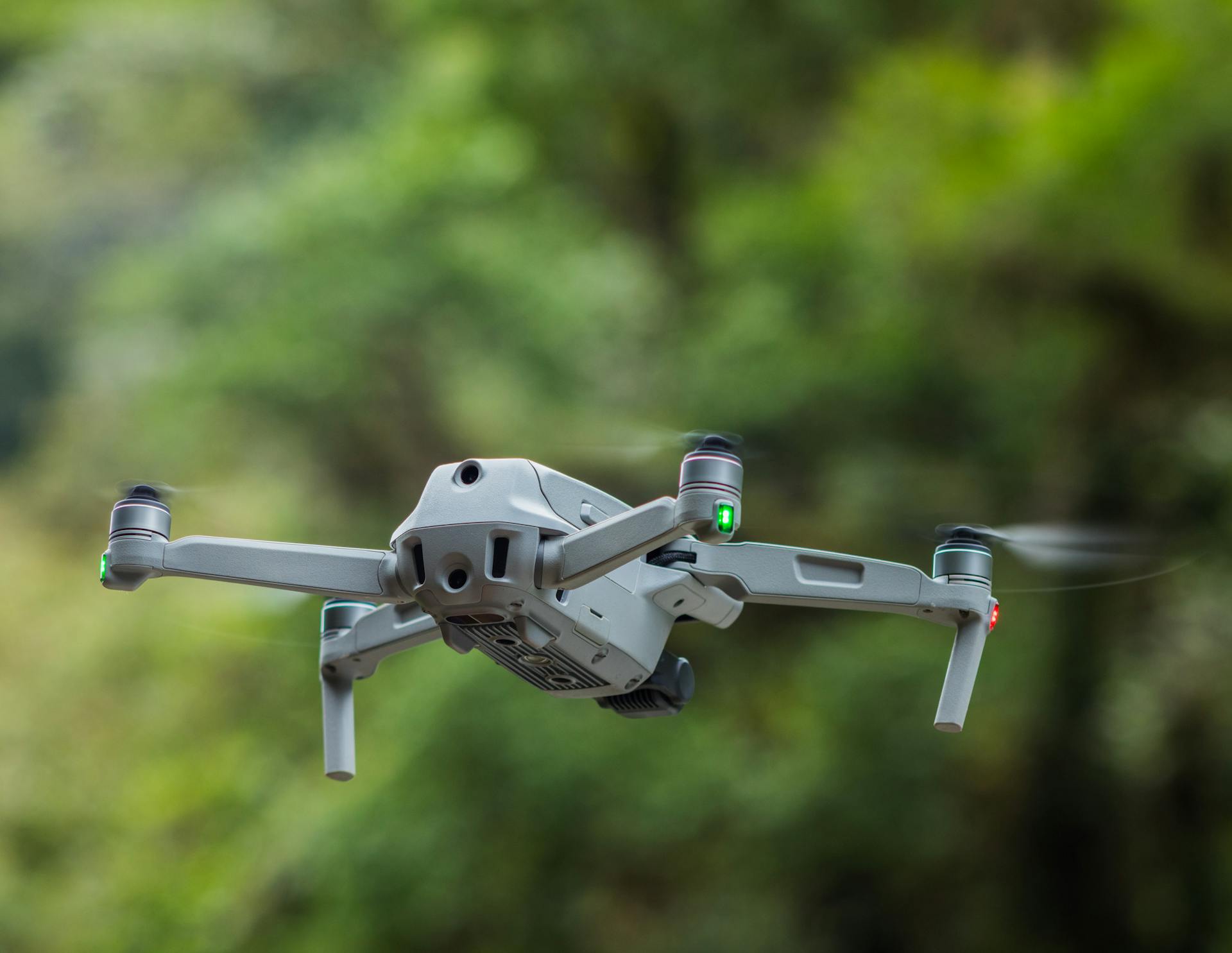 Close-up view of a modern drone in flight with blurred green nature background.