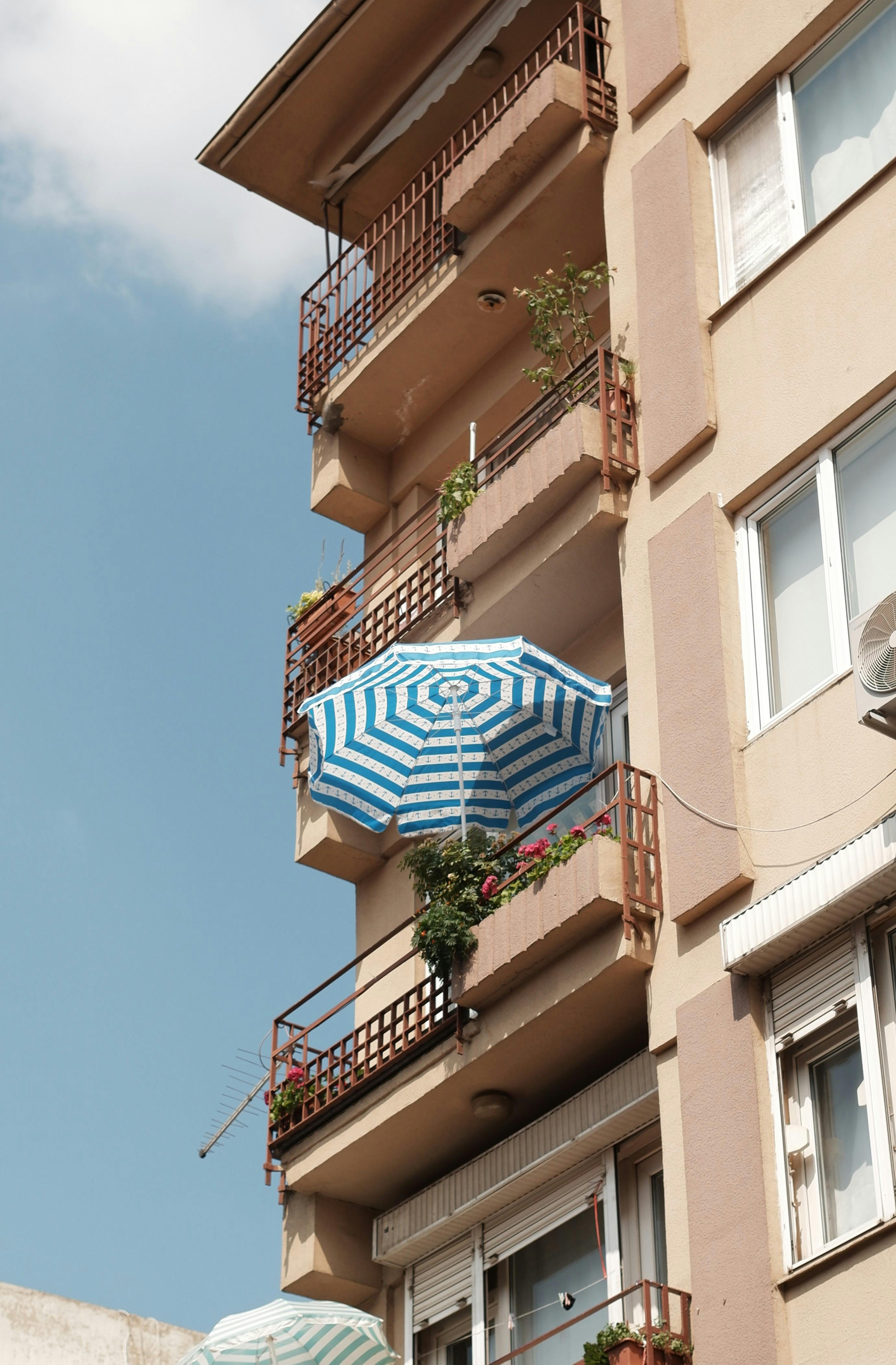 Urban residential building showcasing balconies with vibrant umbrella and plants.