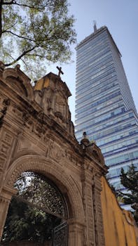 Juxtaposition of historic church entrance and modern skyscraper in Ciudad de México, showcasing architectural contrast.