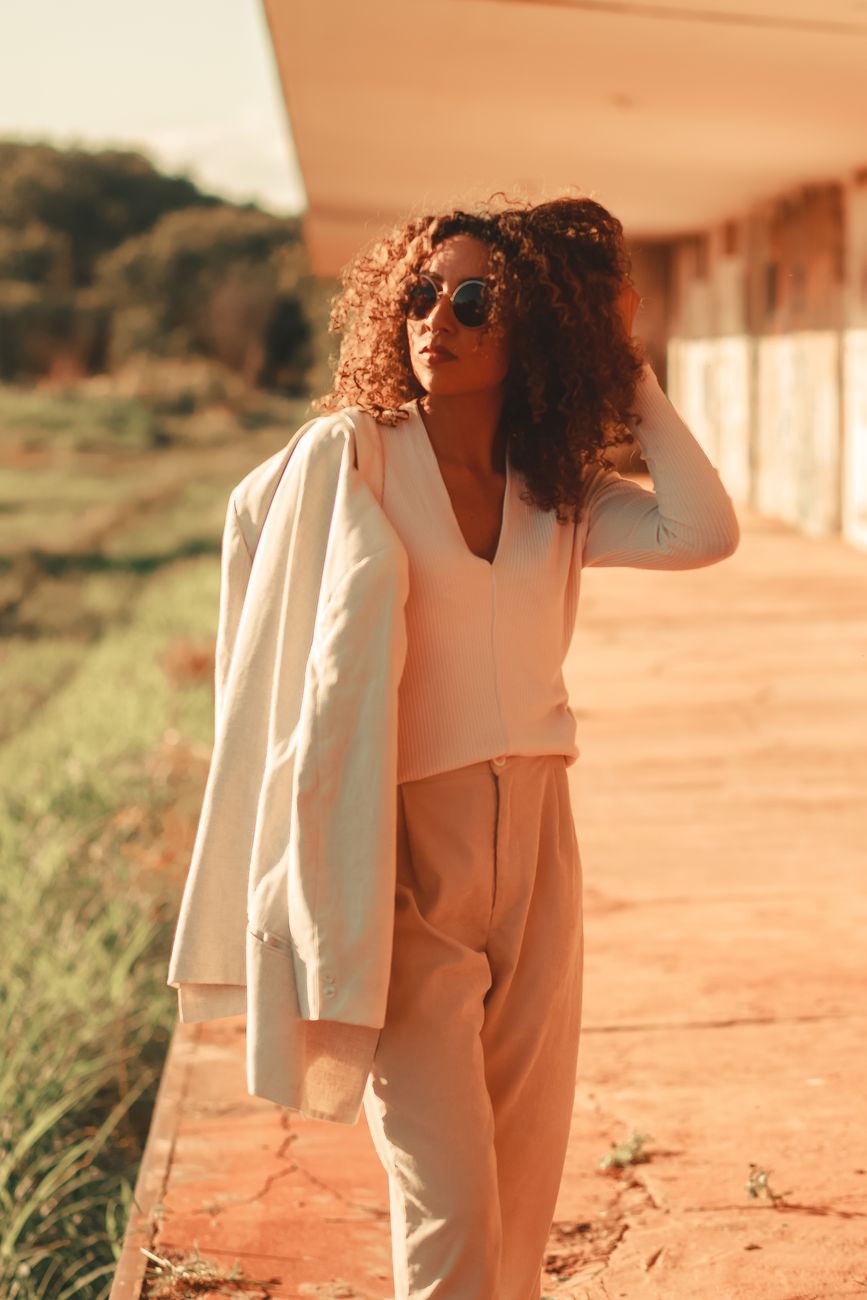 Trendy woman with curly hair poses in stylish outfit outdoors on a sunny day.