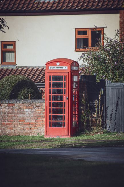 Classic red telephone booth against a quaint village backdrop, evoking nostalgia and history.