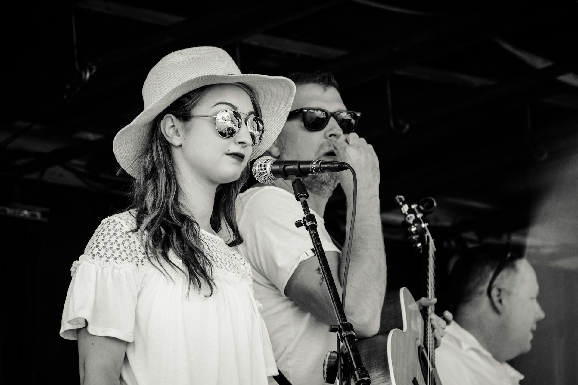 Black and white photo of a live music performance with a female singer in a hat and sunglasses.