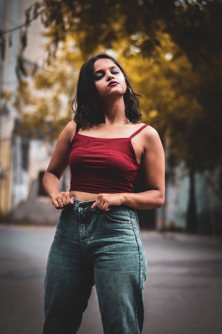 Confident woman posing in casual wear outside with closed eyes against fall backdrop.