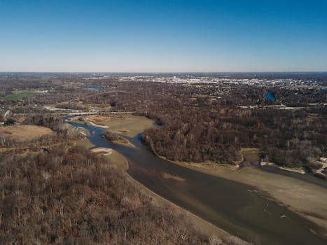 Drone shot capturing a vast autumn forest landscape with a winding river.