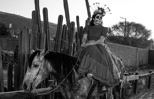 Grayscale Photo of Woman with Face Paint Riding a Horse