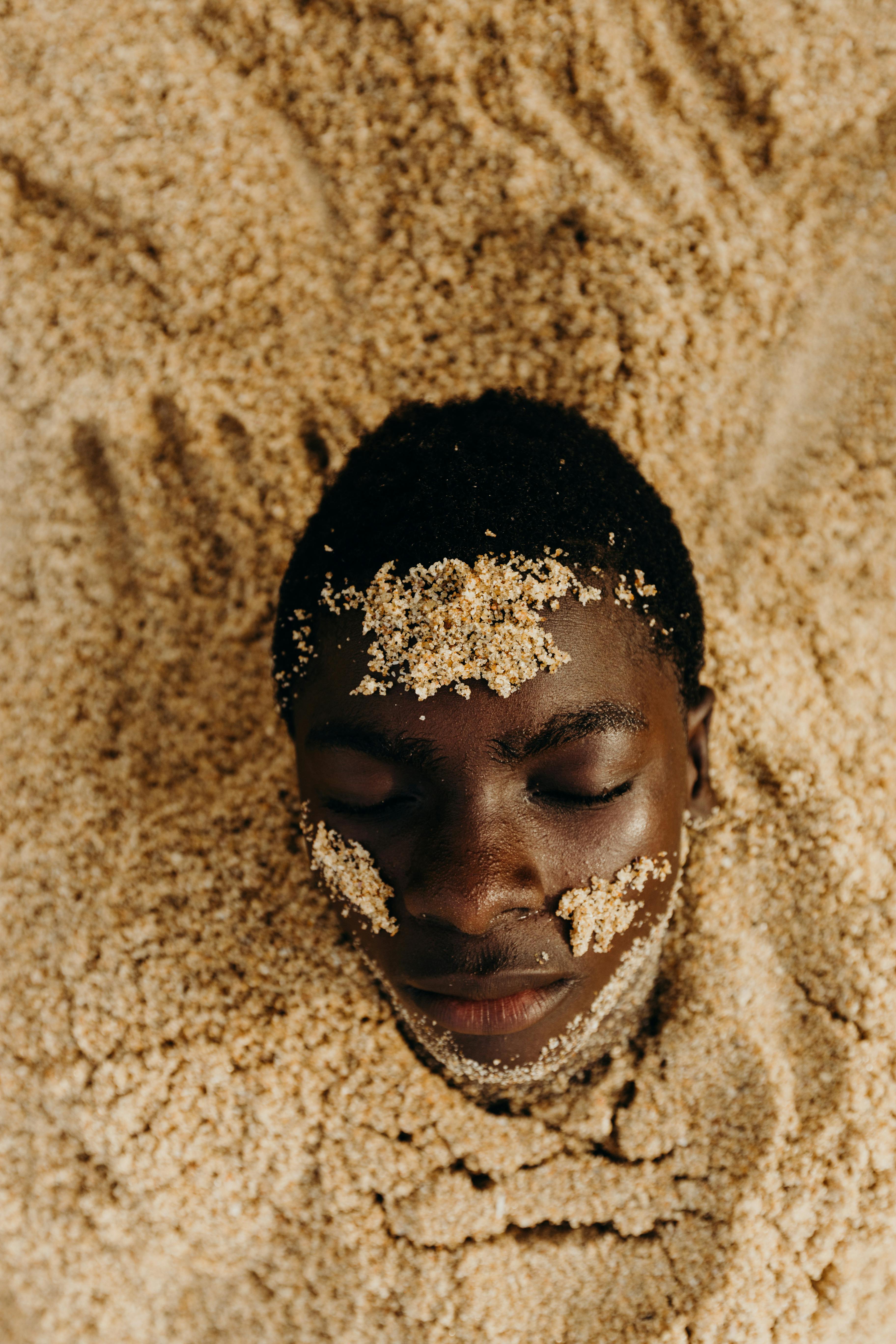 Creative photo of a man's face partially submerged in sand, evoking a sense of calm and artistic expression.