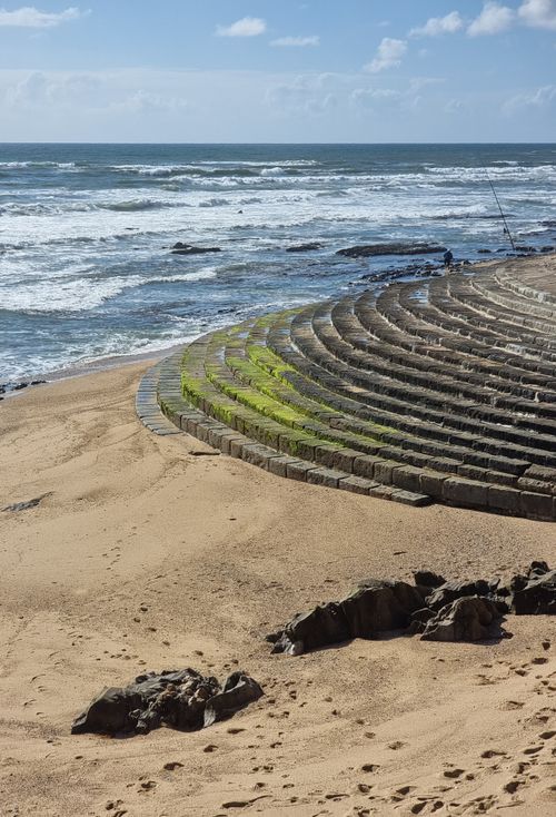 Free An amphitheater along the sandy shoreline of Porto, Portugal with ocean waves in the background. Stock Photo