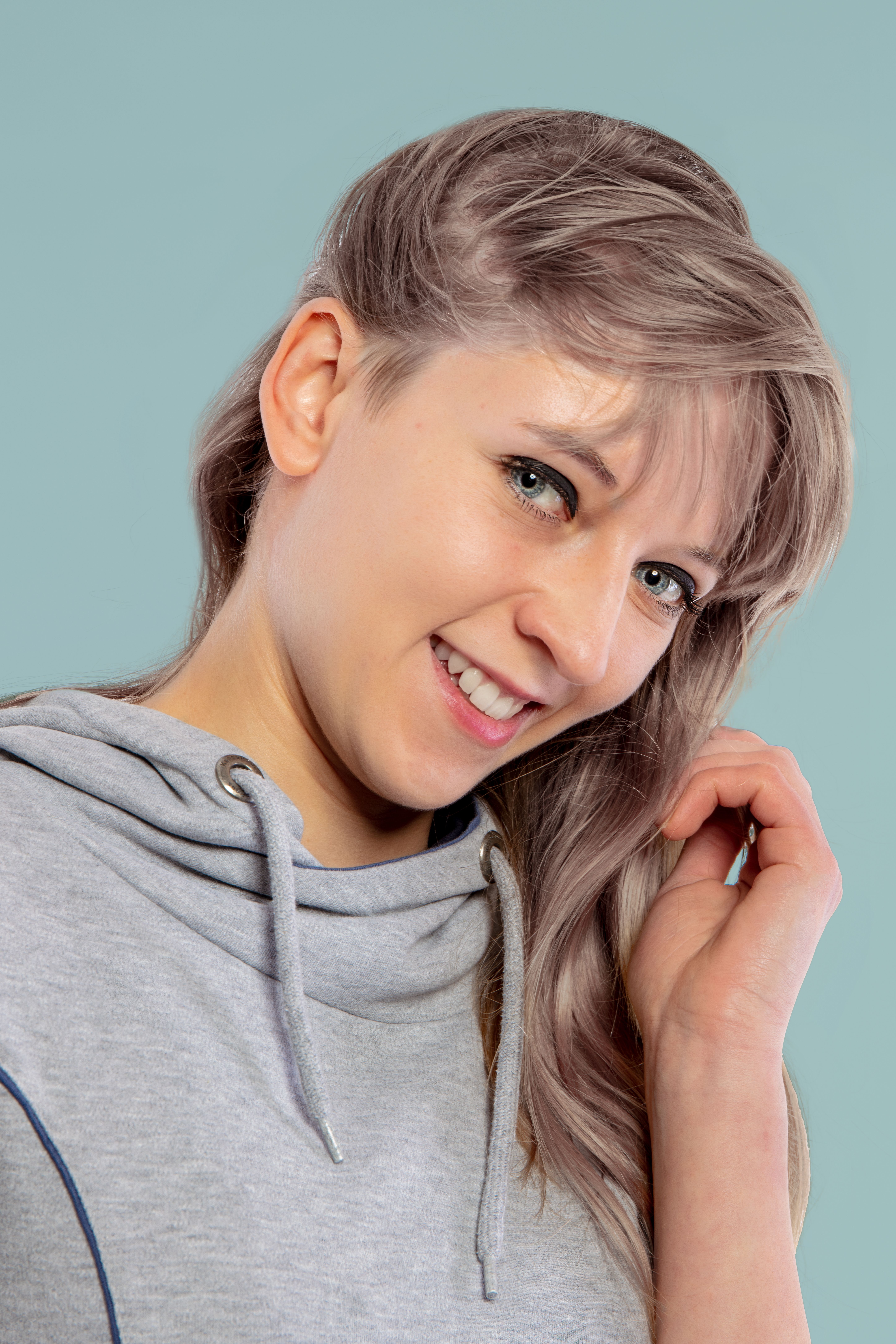 Close-up studio portrait of a smiling young caucasian woman in a grey sweater against a pastel background.