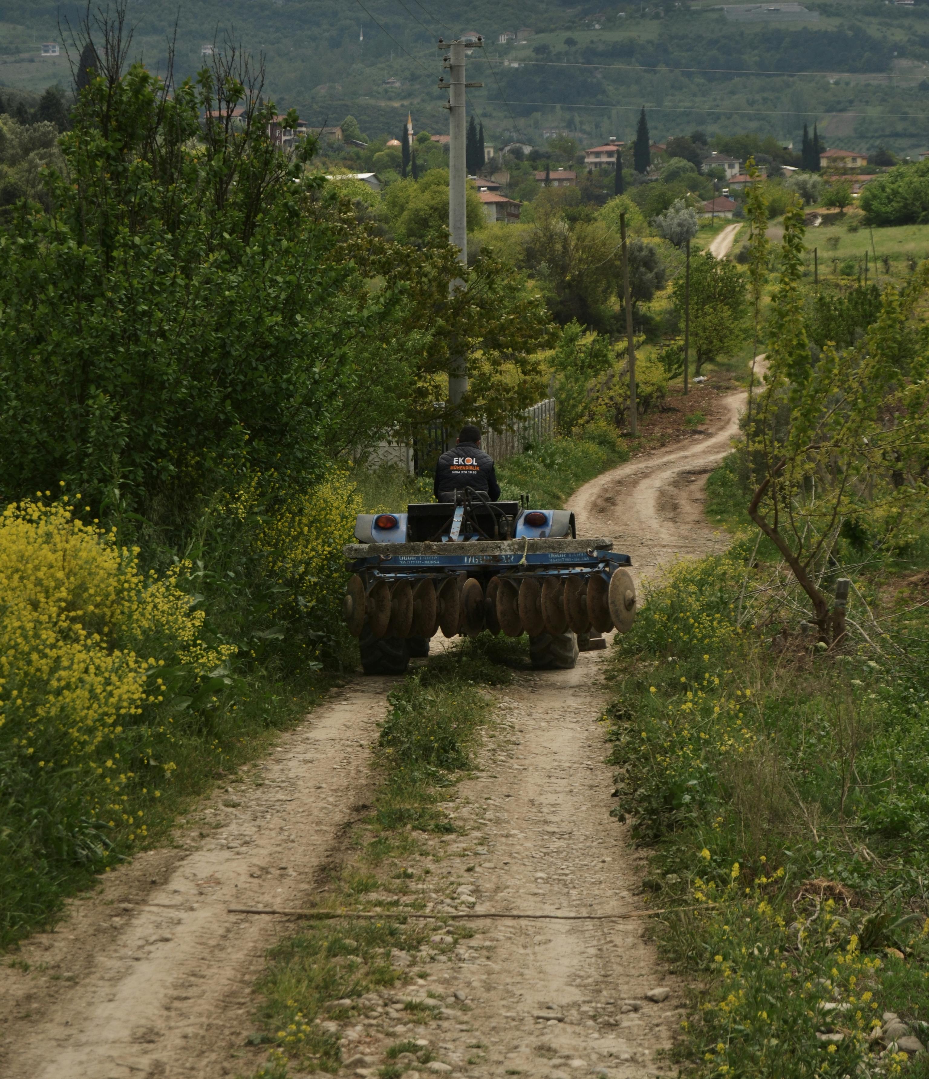 A tractor drives down a rural dirt road in Sakarya, Turkey, amidst lush greenery.