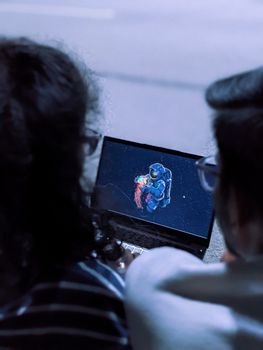 Two people watching an animated astronaut scene on a laptop screen outdoors.