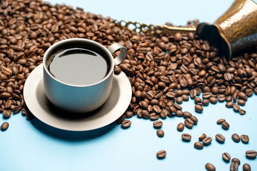 Close-Up Photo of Roasted Coffee Beans Near a Cup of Coffee