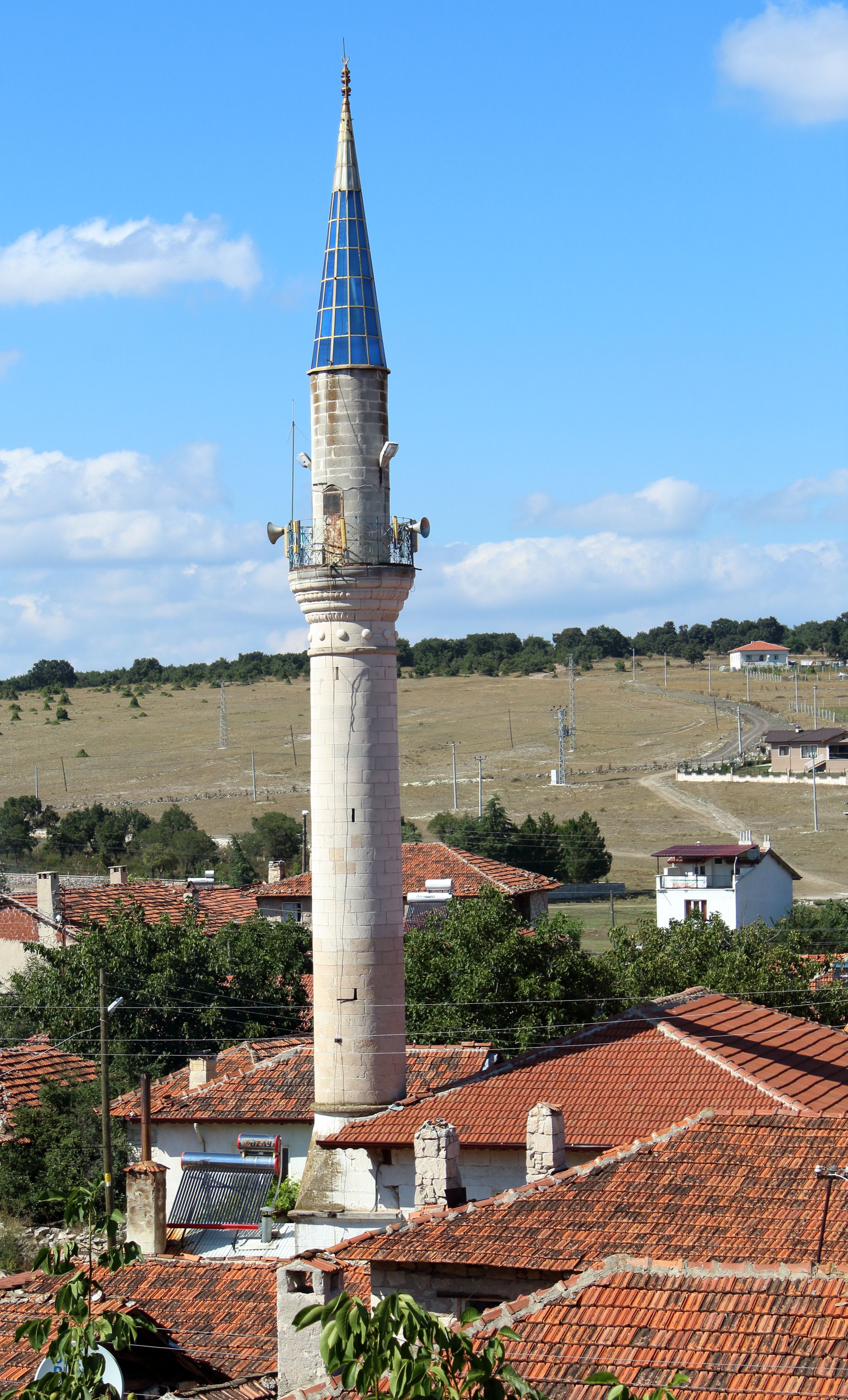 A picturesque mosque minaret rises above village rooftops surrounded by nature in a rural setting.