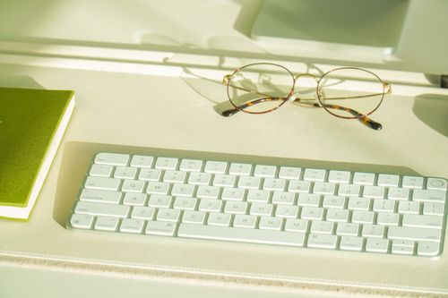 Free Sleek desk setup featuring keyboard, green notebook, and glasses. Ideal for productivity themes. Stock Photo