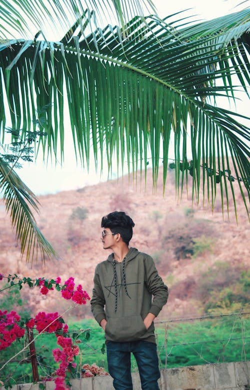 A Guy Standing Near Coconut Tree And Mountains