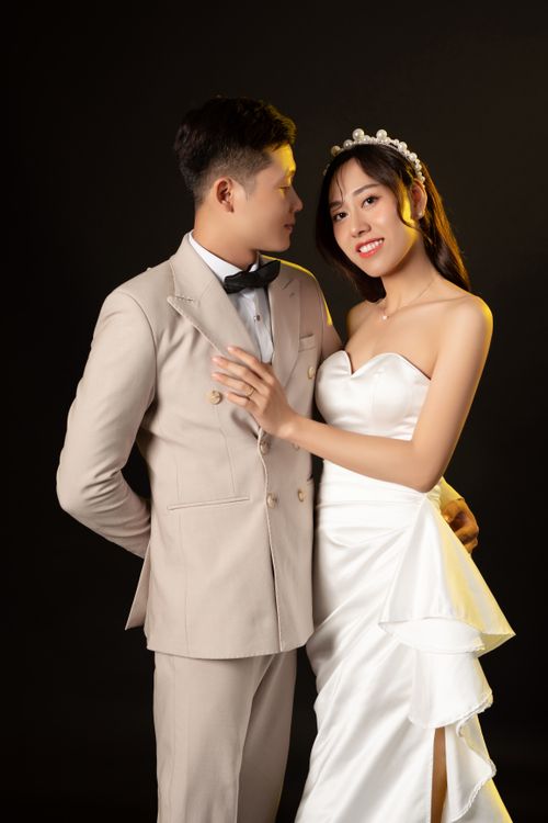 Free Studio portrait of an elegant couple embracing in wedding attire against a dark backdrop. Stock Photo