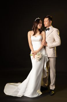 A loving Asian couple in elegant wedding attire gazing at each other romantically.