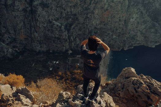 A young man stands on a rocky cliff overlooking a deep canyon, embracing the adventurous view.