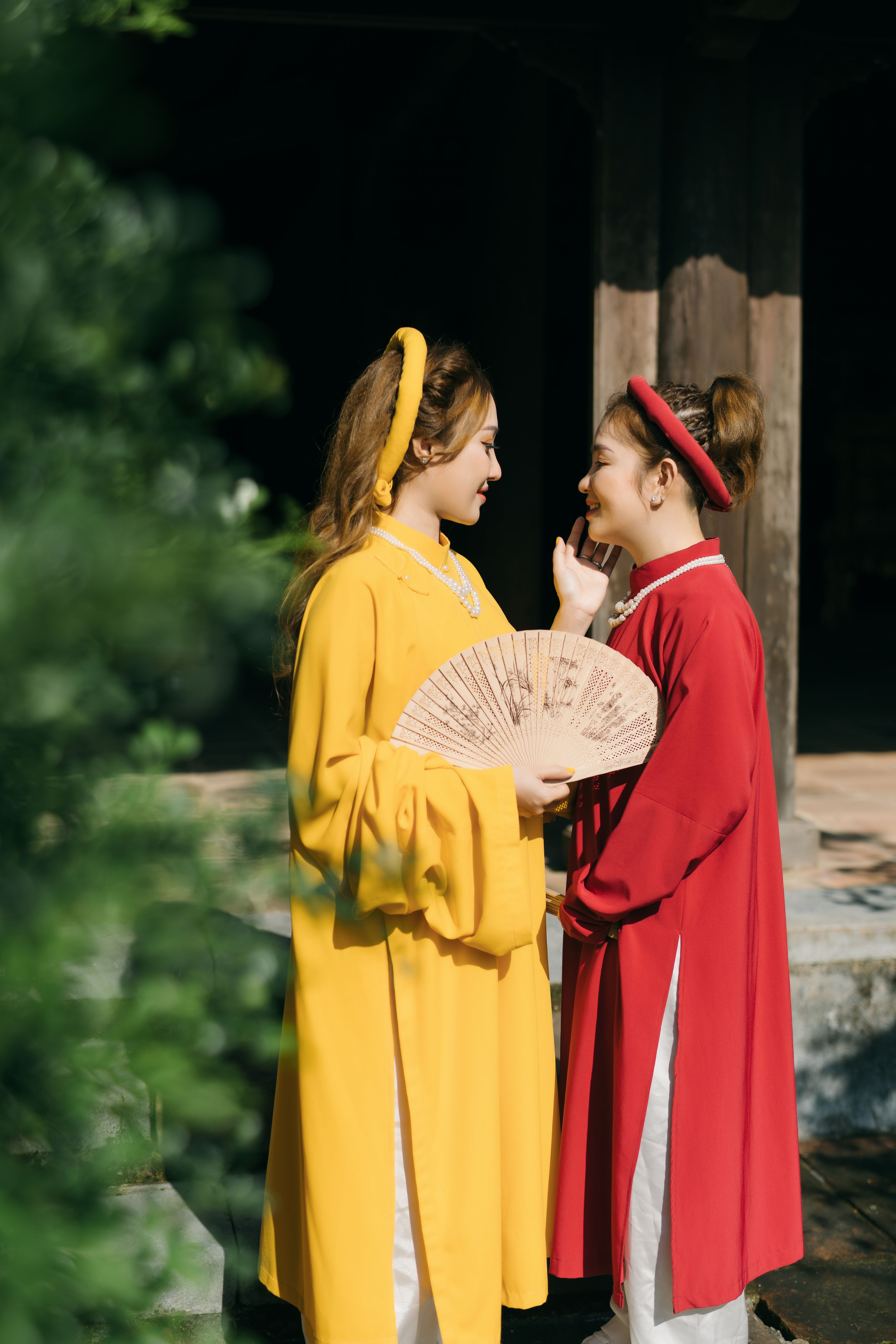 Two women in vibrant traditional outfits standing outdoors, smiling warmly.